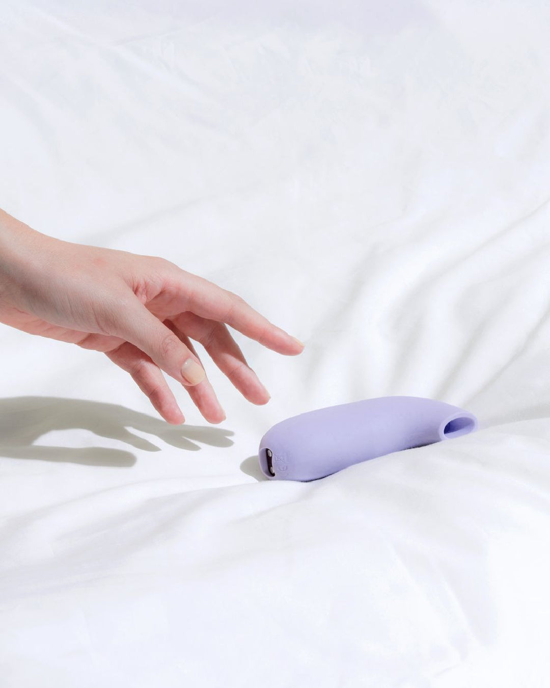 Aer Clitoral Suction Toy Vibrator by Dame Products hand reaching for product on bed