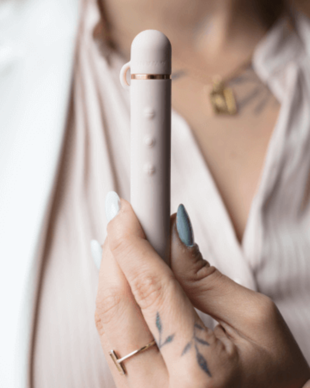 Le Wand Baton Slim Rechargeable Waterproof Vibrator - Rose Gold held in a hand in front of a person's chest